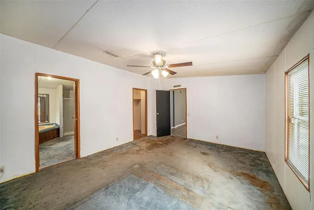 an empty room with chandelier fan and windows