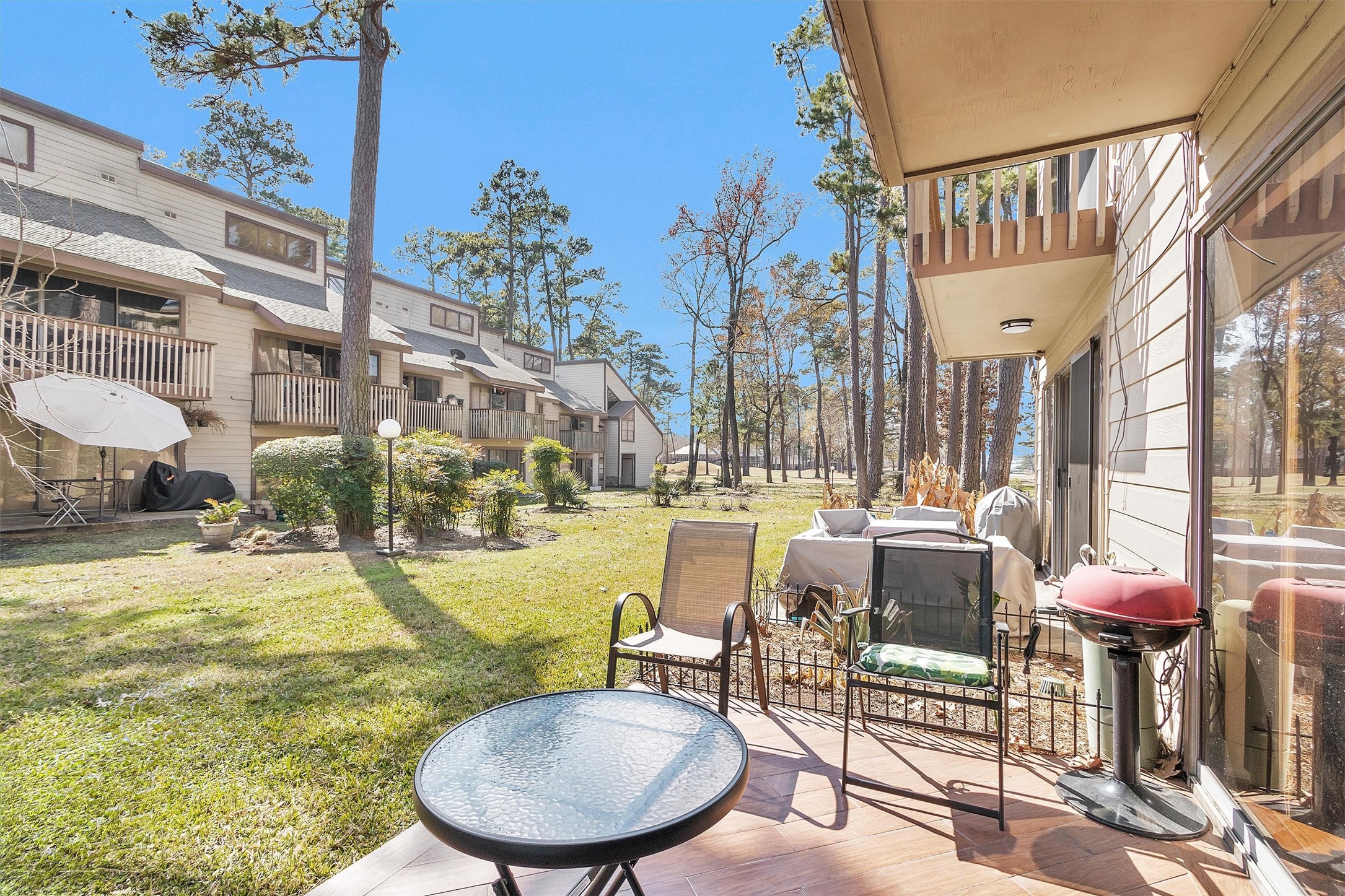 12900 Walden Road, Unit D 411 Montgomery, TX 77356 - Photo 16 of 18 Discover a charming outdoor patio perfect for relaxation or entertaining, overlooking a lush communal yard with serene tree-lined views, complemented by the rustic charm of neighboring townhomes that enhance the community's inviting atmosphere.