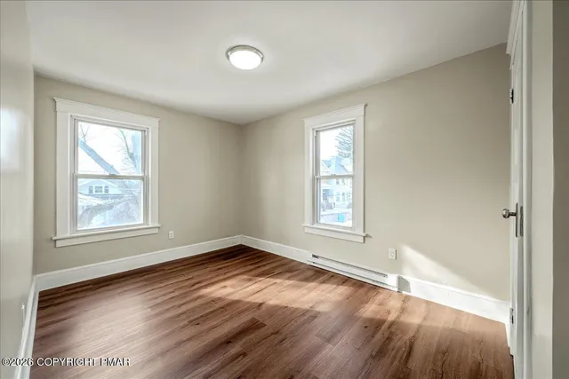 a view of an empty room with wooden floor and window
