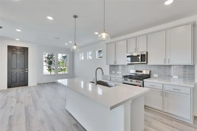 a kitchen with stainless steel appliances granite countertop a sink a stove a refrigerator cabinets and living room view