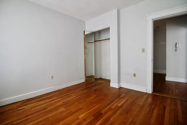 a view of an empty room with wooden floor and closet