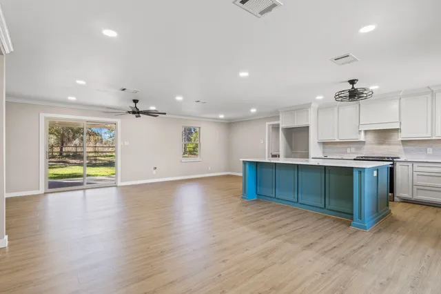 an empty room with wooden floor and kitchen view