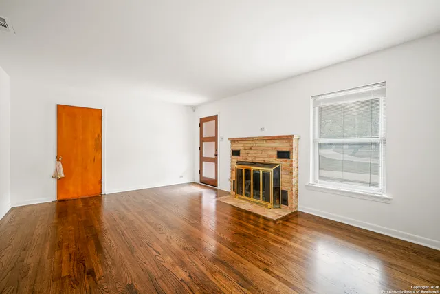 an empty room with wooden floor fireplace and windows