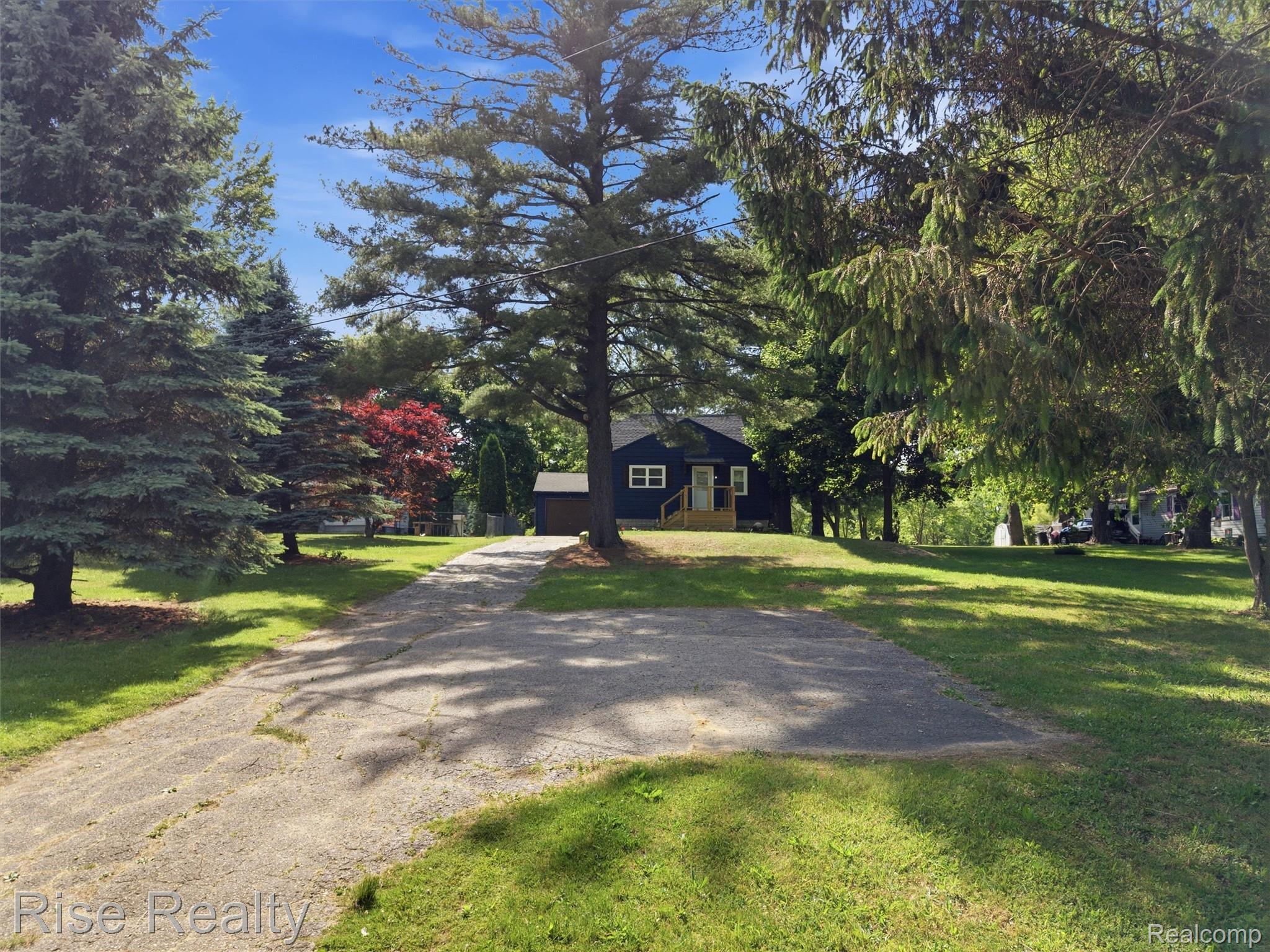2449 North Genesee Road Burton, MI 48509 - Photo 37 of 40 Dark blue siding residence with white window trim and a light wood porch, set on a graded lawn with mature trees