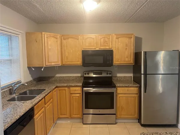 a view of a refrigerator in kitchen and an empty room with wooden floor