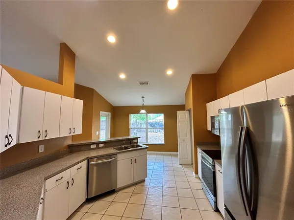 a large kitchen with a large counter top a sink a refrigerator and cabinets
