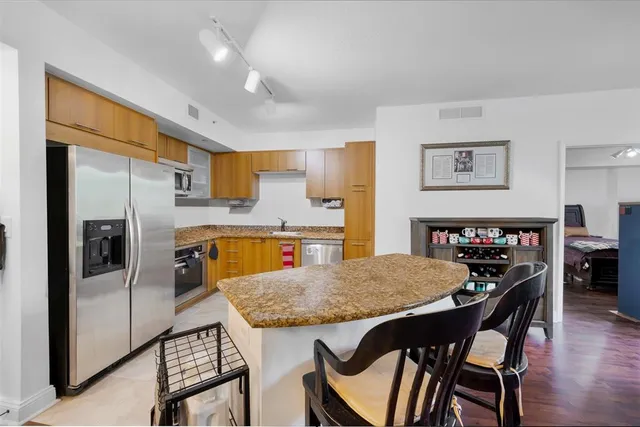 a kitchen with stainless steel appliances granite countertop a dining table chairs refrigerator and sink