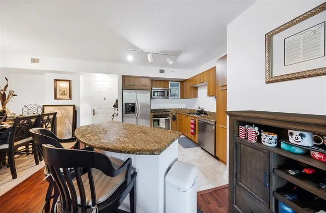 a kitchen with stainless steel appliances granite countertop a stove top oven a sink a dining table and chairs with wooden floor