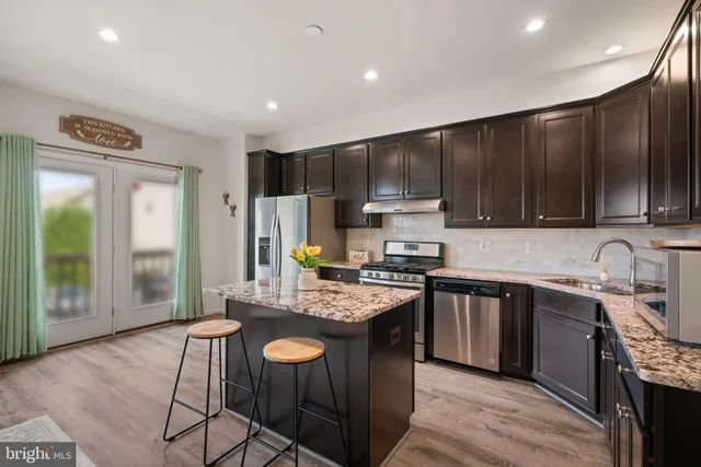 a kitchen with kitchen island granite countertop a sink a stove a refrigerator cabinets and wooden floor