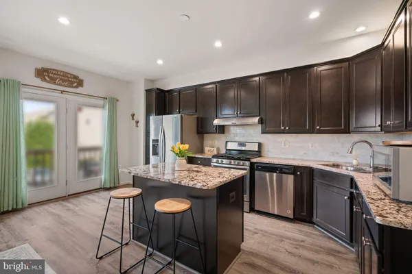 a kitchen with kitchen island granite countertop a sink a stove a refrigerator cabinets and wooden floor