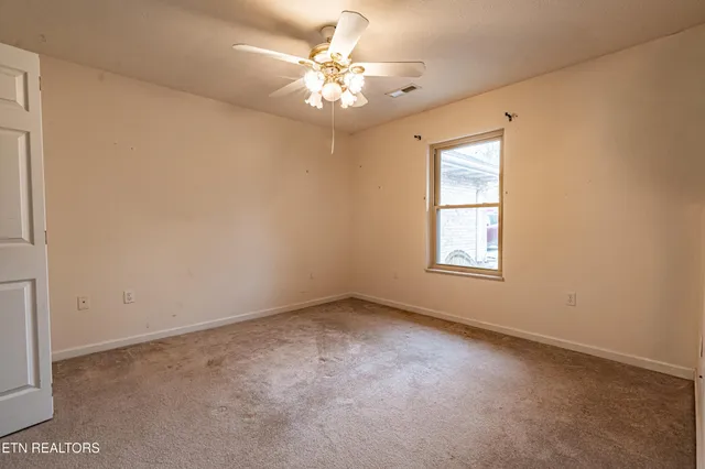an empty room with a chandelier fan and windows