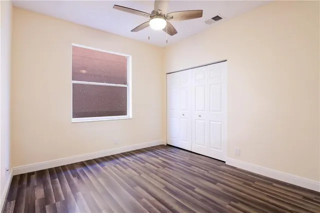 a view of an empty room with wooden floor and a ceiling fan