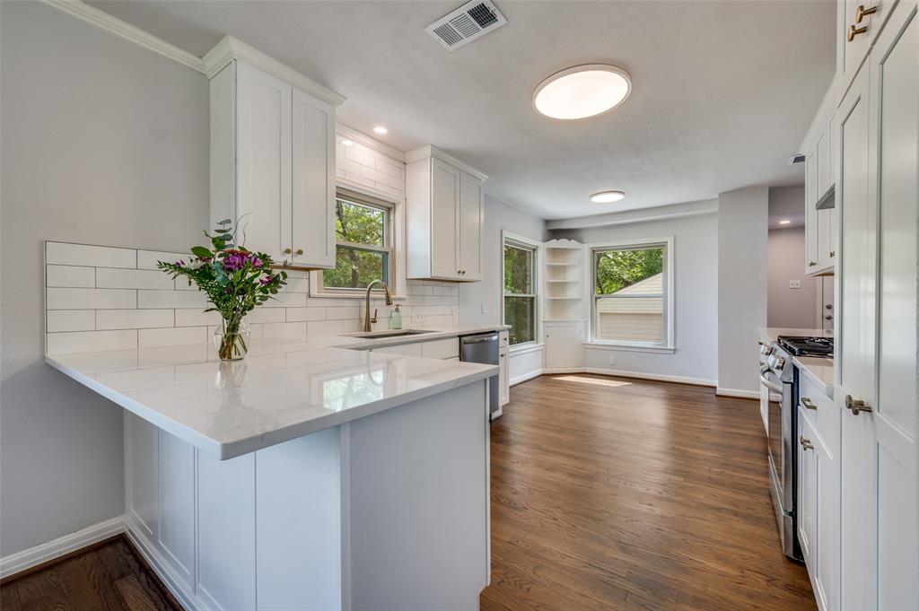 1342 Michigan Avenue Dallas, TX 75216 - Photo 12 of 25 Kitchen with a peninsula, backsplash, white cabinets, stainless steel appliances, and dark wood-style flooring