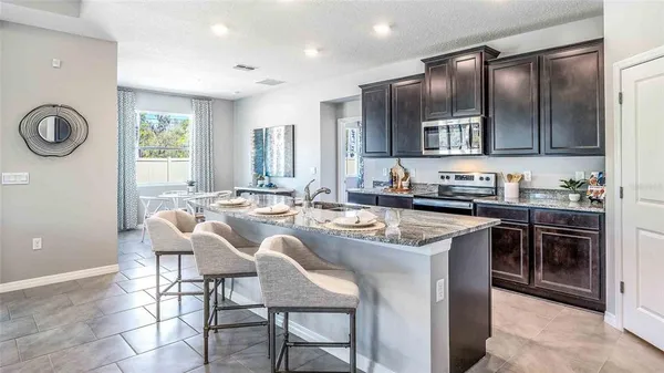 a kitchen with granite countertop a sink a stove a refrigerator cabinets and chairs