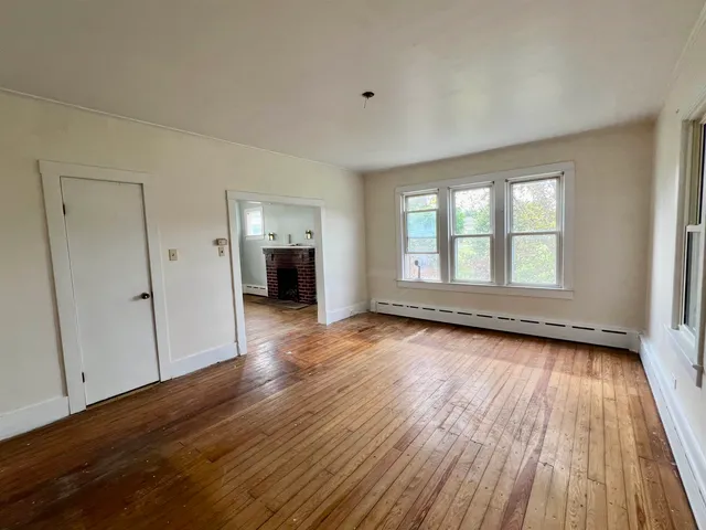a view of an empty room with a window and wooden floor