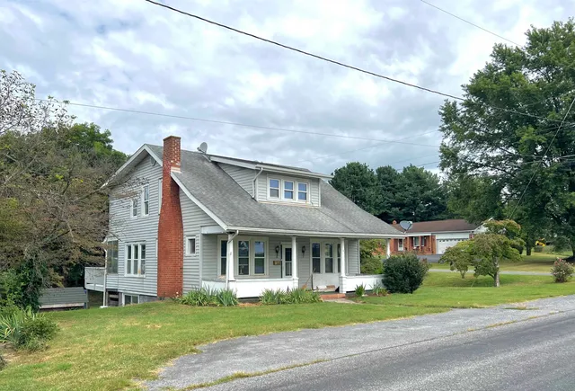 a view of a white house next to a yard with big trees