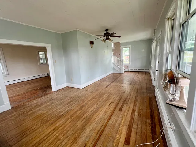 an empty room with wooden floor chandelier fan and windows