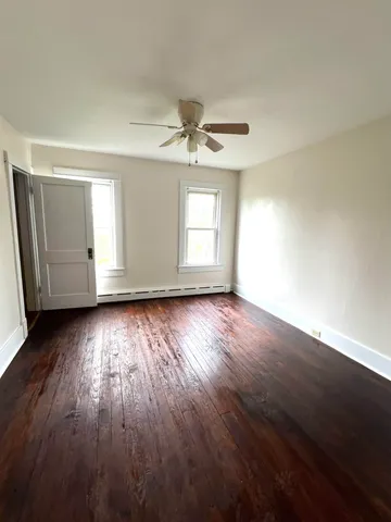an empty room with wooden floor fan and windows