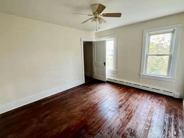 an empty room with wooden floor chandelier fan and windows