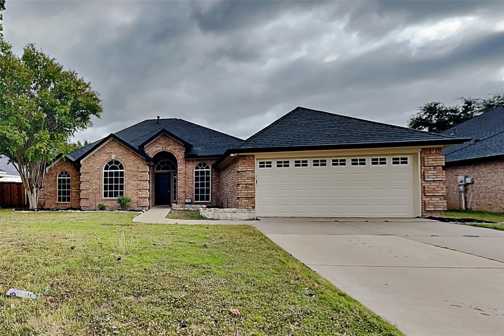 View of front facade featuring a shingled roof, concrete driveway, brick siding, a front lawn, and an attached garage
