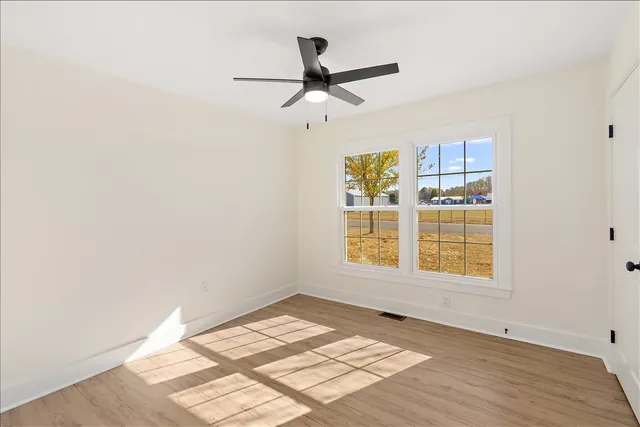 an empty room with wooden floor fan and windows