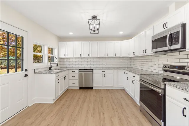 a kitchen with granite countertop a stove top oven a sink dishwasher and white cabinets with wooden floor