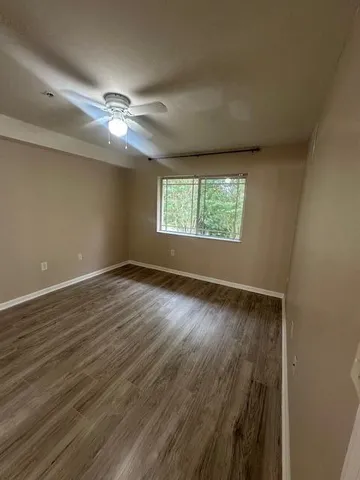 an empty room with wooden floor fan and windows