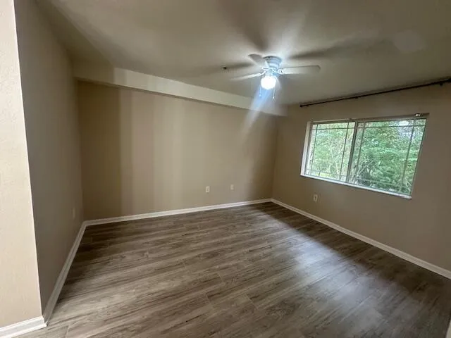 a view of an empty room with wooden floor and a ceiling fan