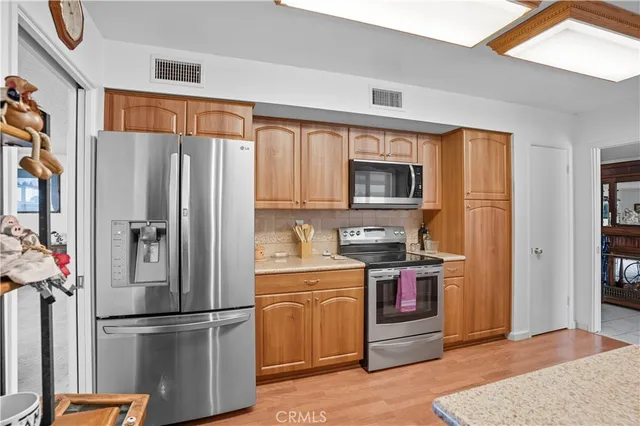 a kitchen with stainless steel appliances granite countertop a refrigerator a sink dishwasher a stove and white countertops with wooden floor