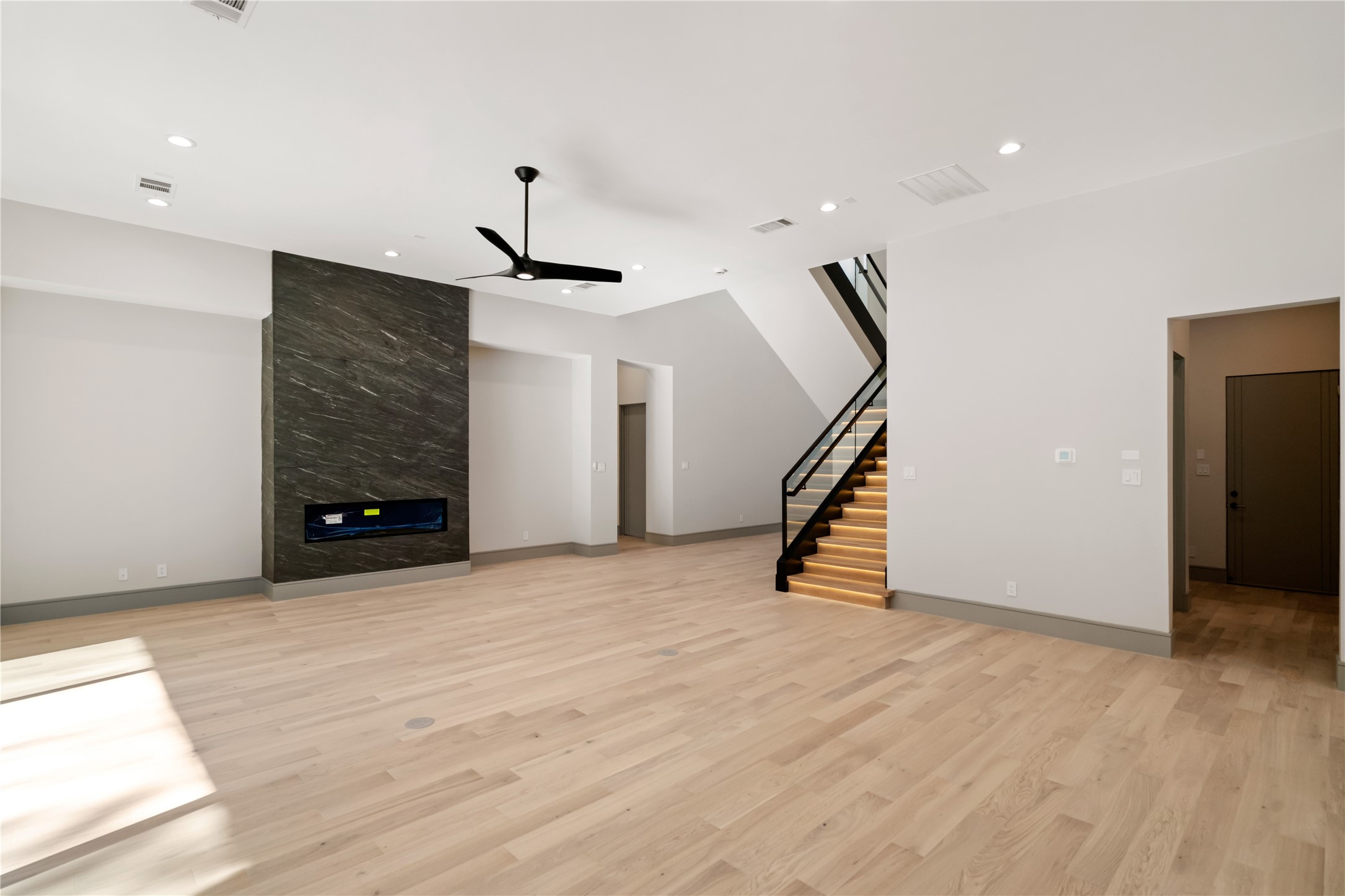 47 Pronghorn Place Spring, TX 77389 - Photo 20 of 44 Spacious modern living area with light wood flooring, a sleek black fireplace, recessed lighting, and a striking staircase with illuminated steps. Perfect for contemporary living.