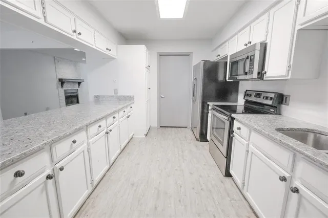 a kitchen with stainless steel appliances granite countertop a sink a stove a refrigerator and white cabinets