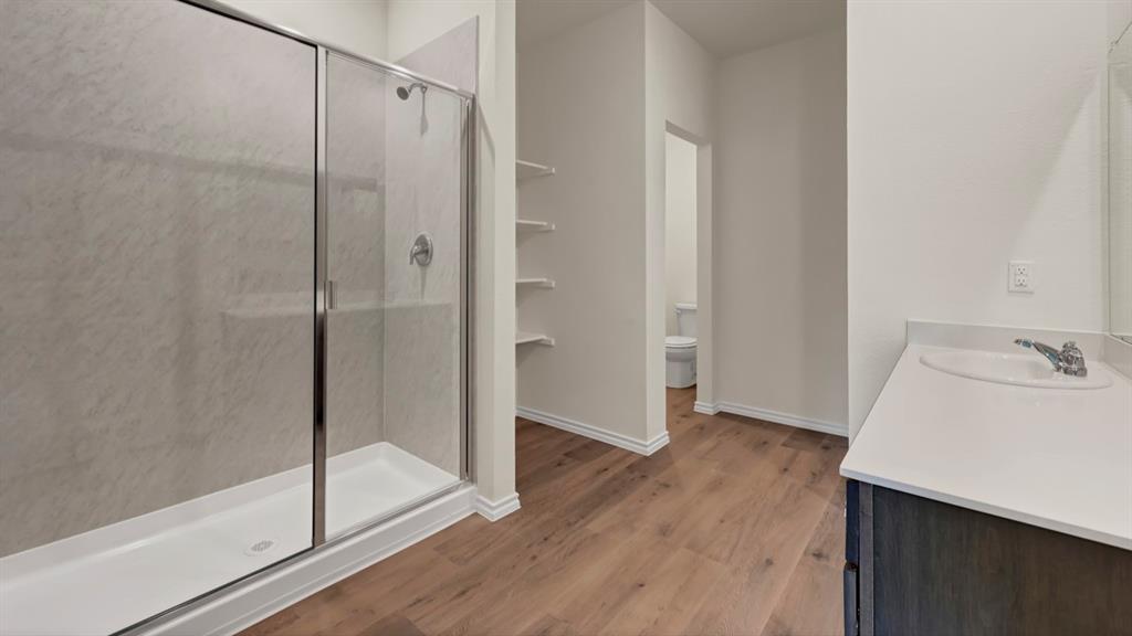 4012 Ripplewood Drive Lindale, TX 75771 - Photo 30 of 37 Spacious bathroom featuring a glass-enclosed shower with a textured surround, wood-finish flooring, a contemporary vanity with an integrated sink and light-toned countertop, and built-in shelving