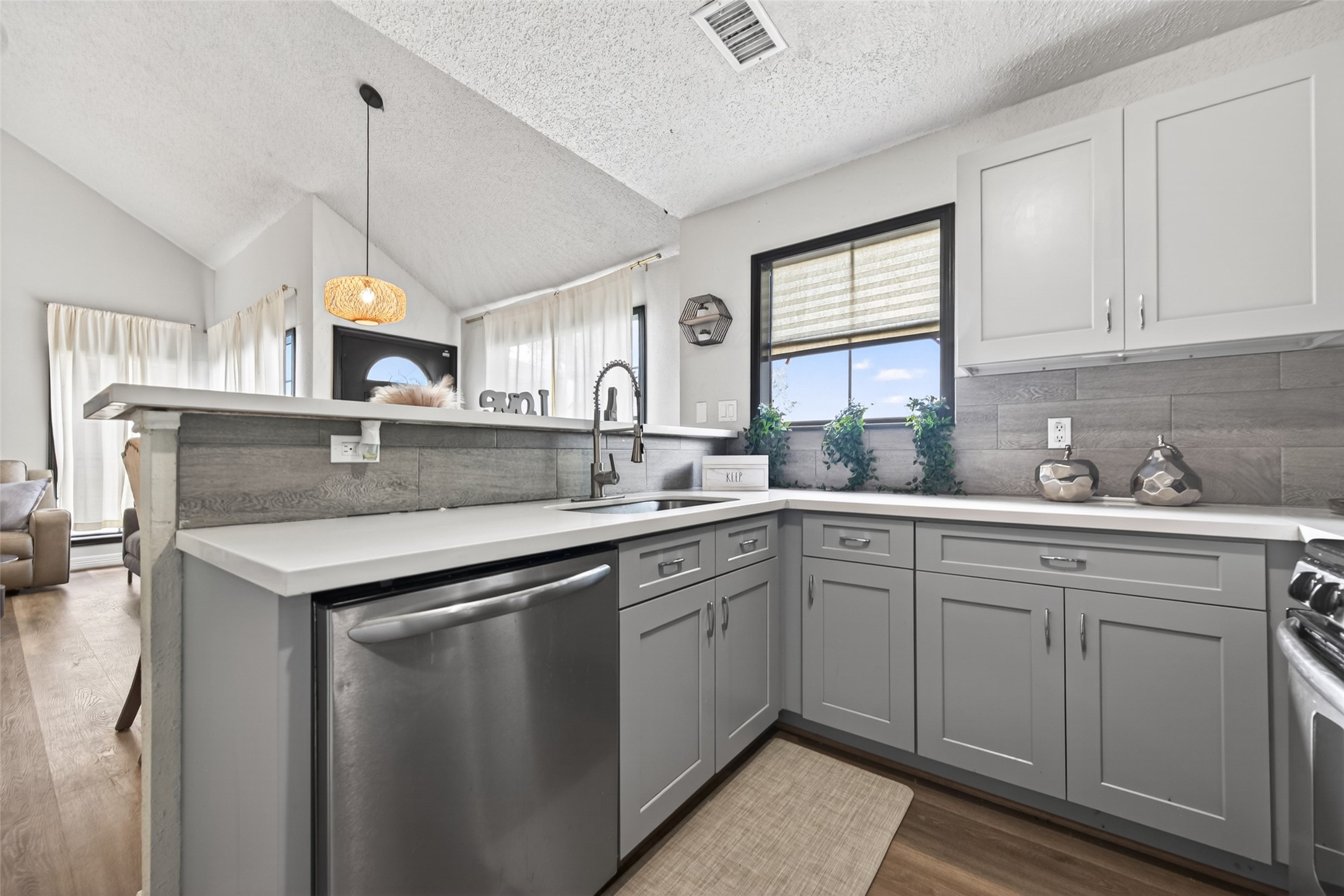 18446 North Willow Bluff Road Katy, TX 77449 - Photo 14 of 33 This kitchen features modern gray cabinetry, stainless steel appliances, and a stylish tile backsplash. The open layout connects to a cozy living space with abundant natural light, creating a welcoming atmosphere.