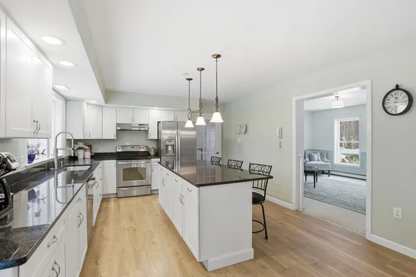 a kitchen with stainless steel appliances kitchen island granite countertop a stove top oven a sink a dining table and chairs with wooden floor