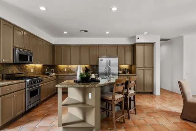 a kitchen with stainless steel appliances a stove a sink a microwave a refrigerator and chairs