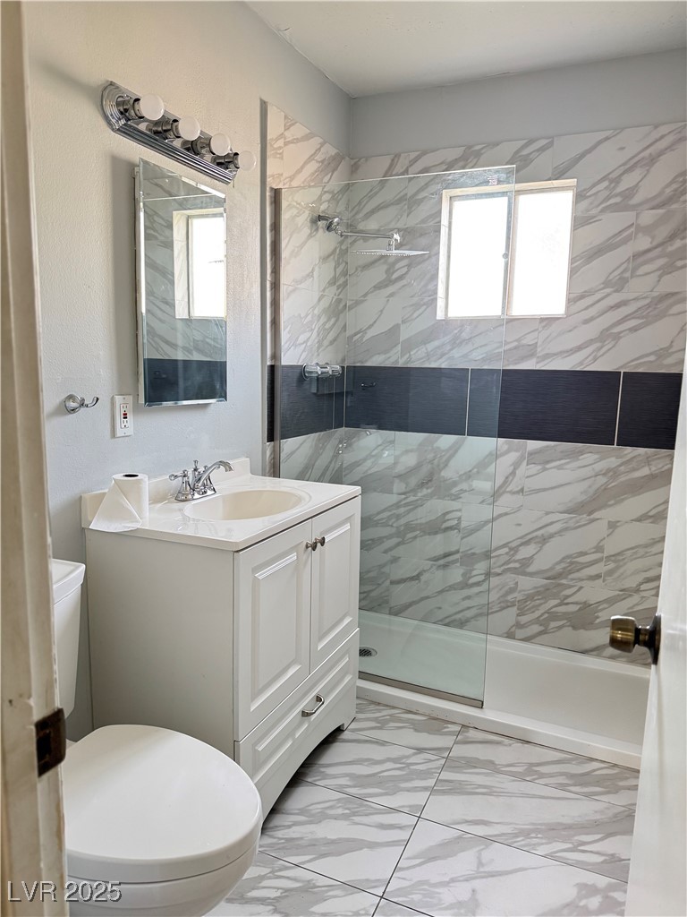 Full bath featuring light marble finish flooring, a walk in shower, and vanity