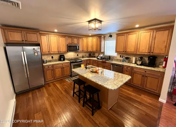 a kitchen with stainless steel appliances granite countertop a refrigerator a sink dishwasher a stove and white countertops with wooden floor