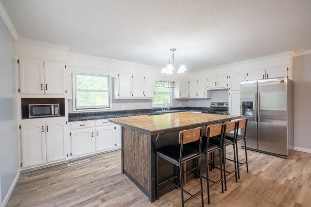 a kitchen with stainless steel appliances granite countertop a stove a sink dishwasher a refrigerator with white cabinets and wooden floor