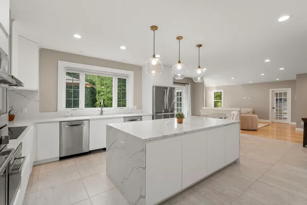 a large white kitchen with a large center island kitchen island a sink a stove and a large window