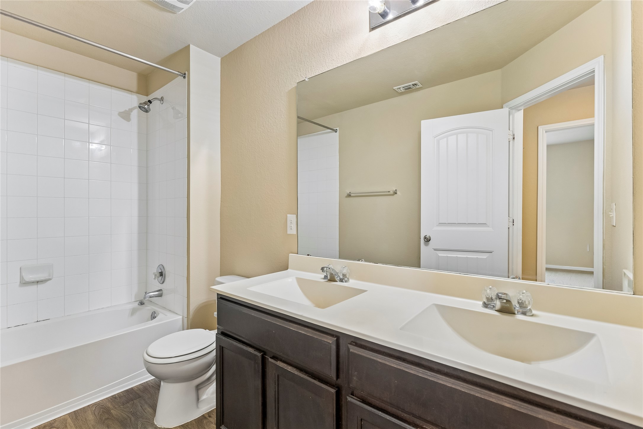 14409 Estuary Road Manor, TX 78653 - Photo 17 of 24 Bathroom featuring a dual vanity with integrated sinks, dark wood-finish cabinetry, a large wall mirror, and wood-finish flooring