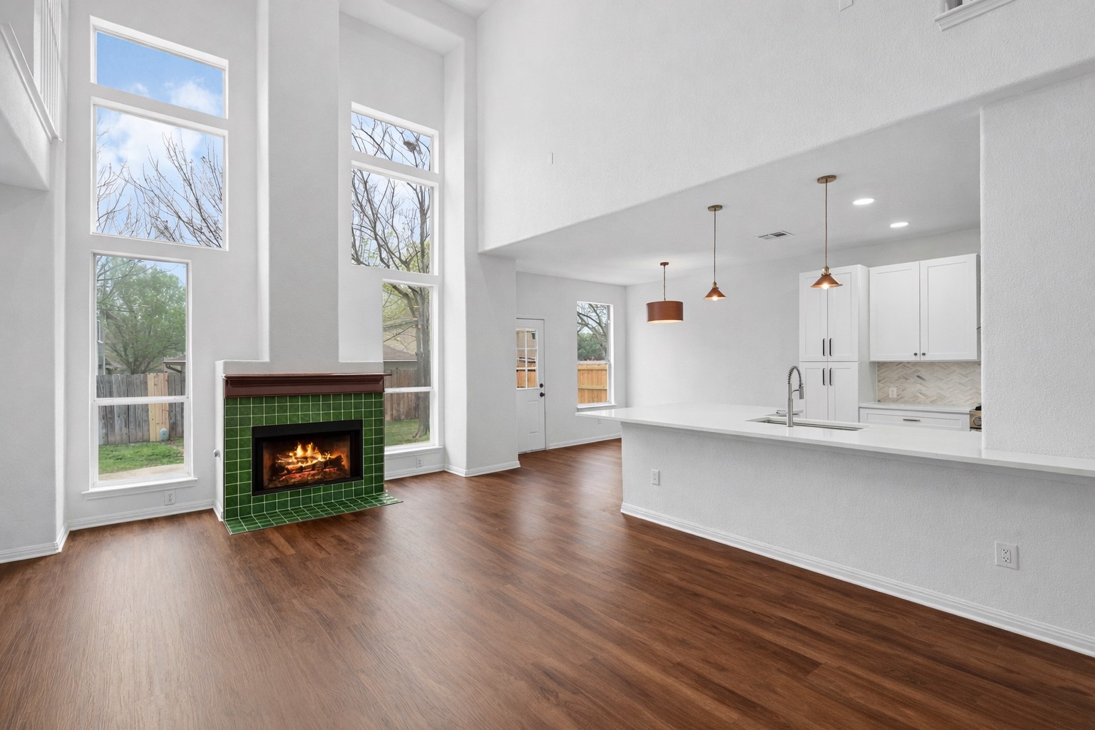 813 Caribou Ridge Trail Pflugerville, TX 78660 - Photo 10 of 39 Light-filled living room with soaring ceilings, floor-to-ceiling windows, a tiled fireplace, and warm luxury vinyl plank flooring.