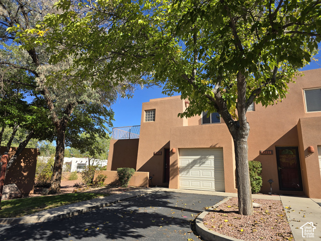 3299 Fairway Loop Moab, UT 84532 - Photo 23 of 23 Stucco exterior finish, attached garage with panel door, front entry with security door, upper-level balcony with metal railing, and a decorative glass block window