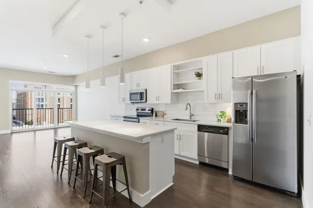 a kitchen with stainless steel appliances a stove a sink a refrigerator white cabinets and wooden floor