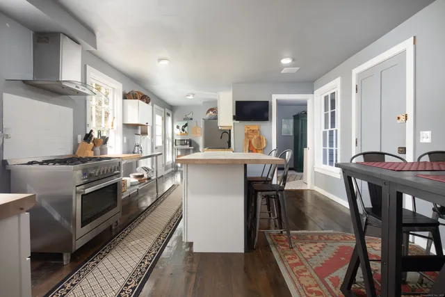 a kitchen with stainless steel appliances granite countertop a stove top oven a sink a dining table and chairs with wooden floor