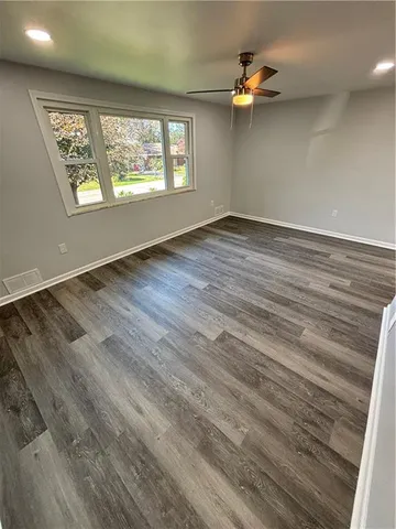 an empty room with wooden floor fan and windows
