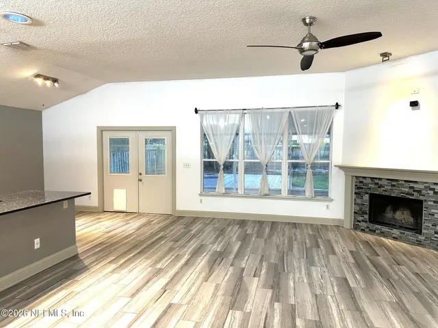 a view of an empty room with wooden floor fireplace and a window
