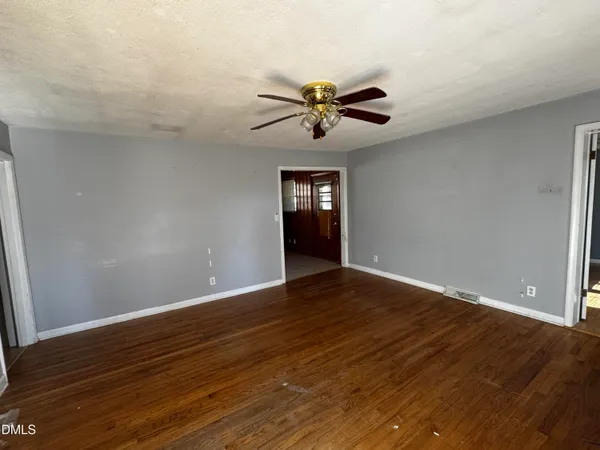 a view of an empty room with wooden floor and a ceiling fan