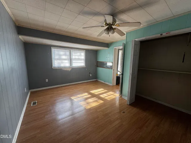 an empty room with wooden floor fan and windows