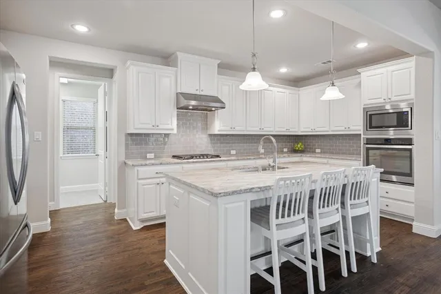 a kitchen with stainless steel appliances granite countertop a kitchen island hardwood floor and a sink