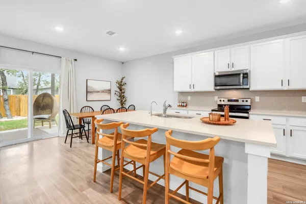 a kitchen with stainless steel appliances granite countertop a stove a sink a refrigerator and white cabinets with wooden floor